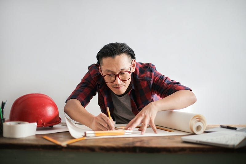 A man hunched over a desk of writing tools, at work.